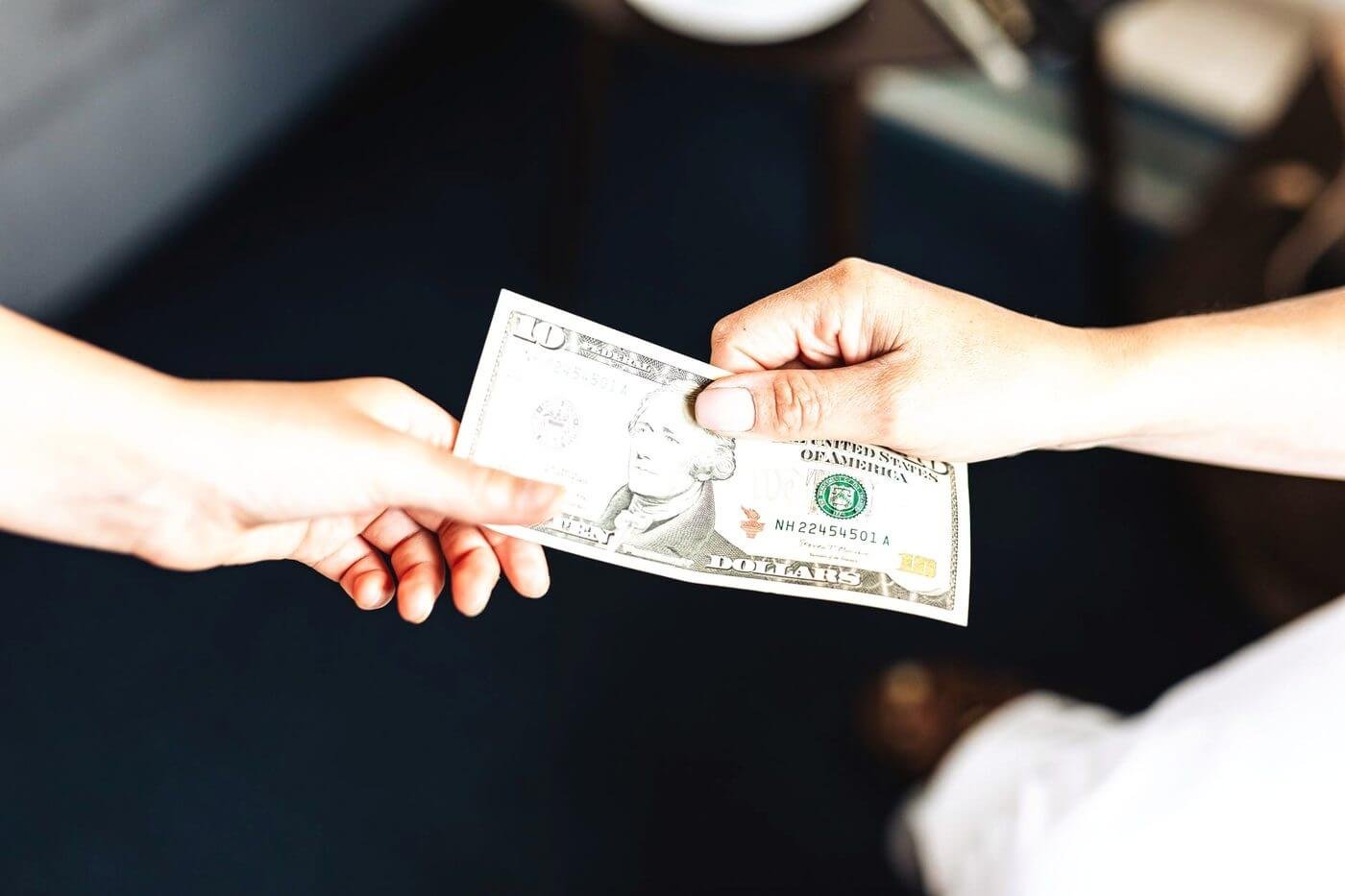 Dos manos pasando un billete de un dólar, sobre un fondo oscuro