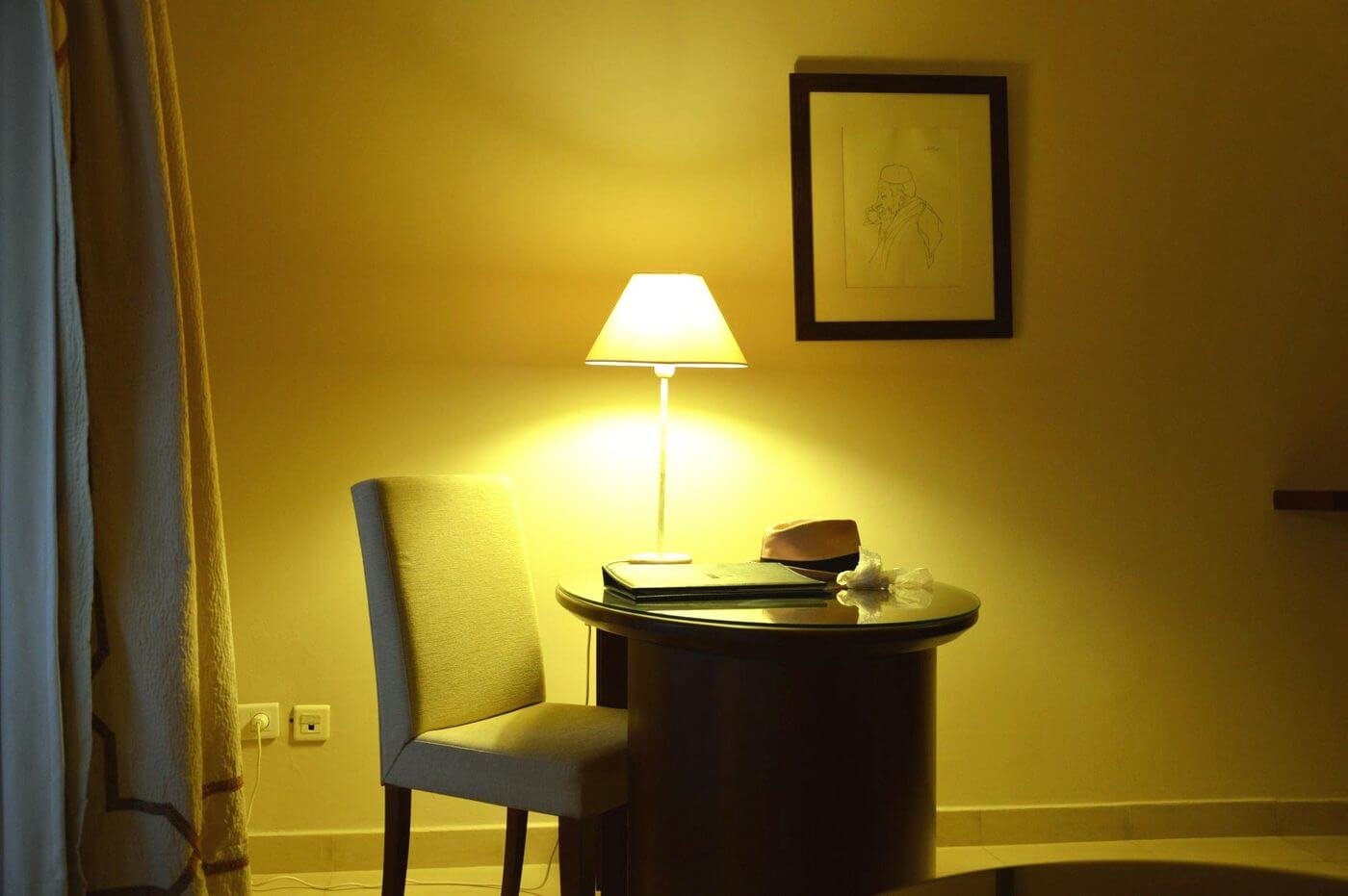 Un cuarto en penumbra con una lámpara encendida sobre una mesa y una silla vacía