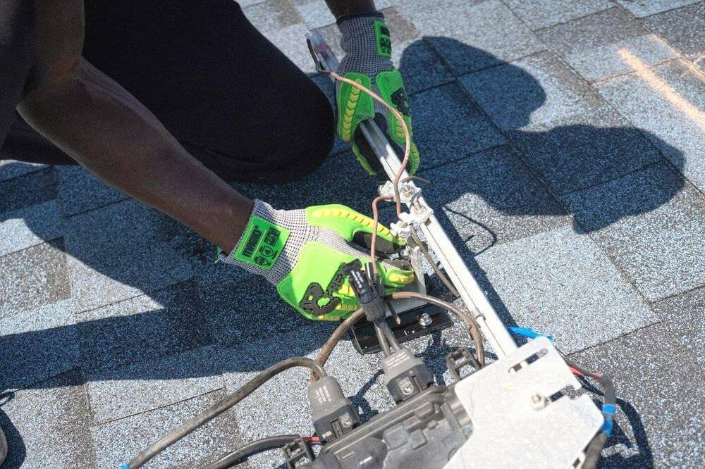 Manos con guantes de trabajo verdes ajustando un perfil y sus cables sobre un techo, a pleno sol